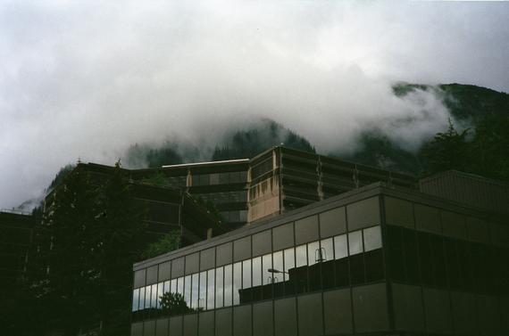 A dramatic photo of a brutalist building with misty mountains in the background