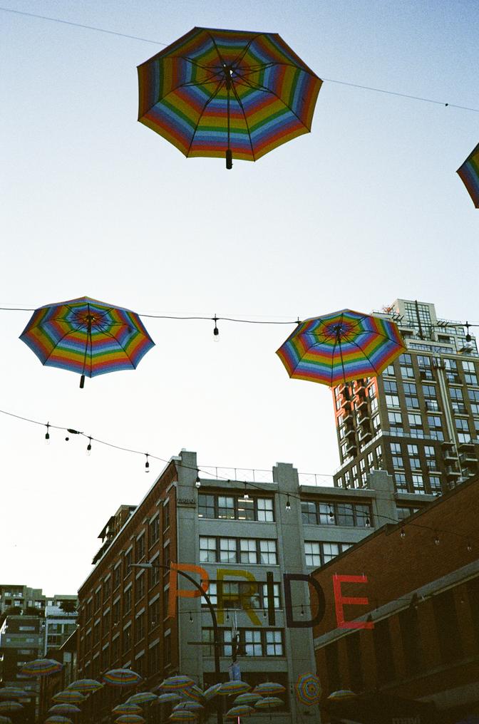 Rainbow umbrellas above a pride sign and string lights