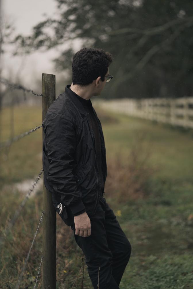 Me leaning against a fence post in a field, looking away