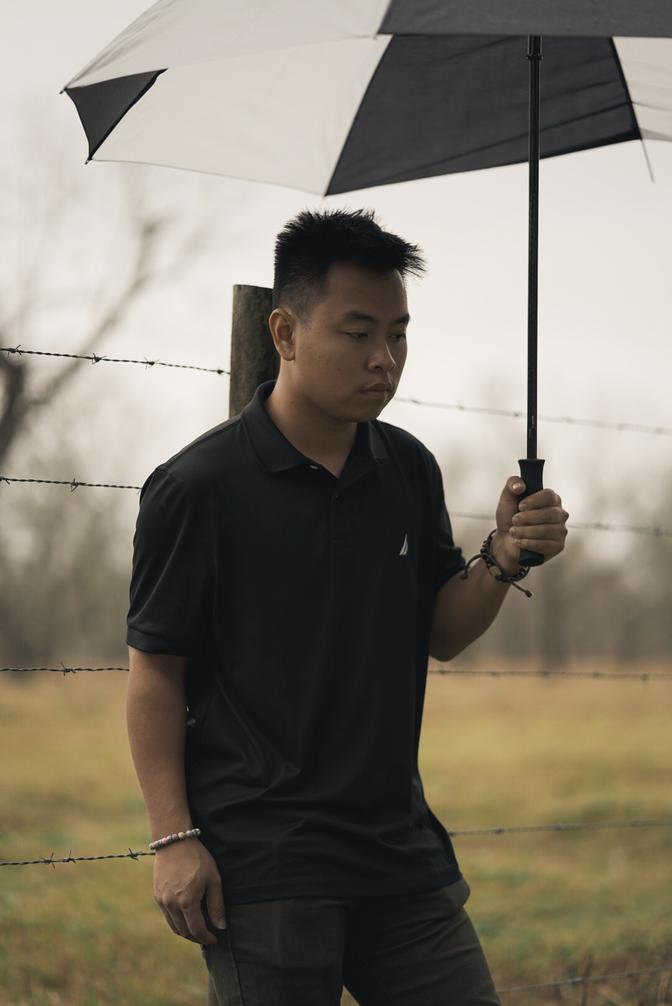 Andrew leaning against a fence post, holding and umbrella and looking down