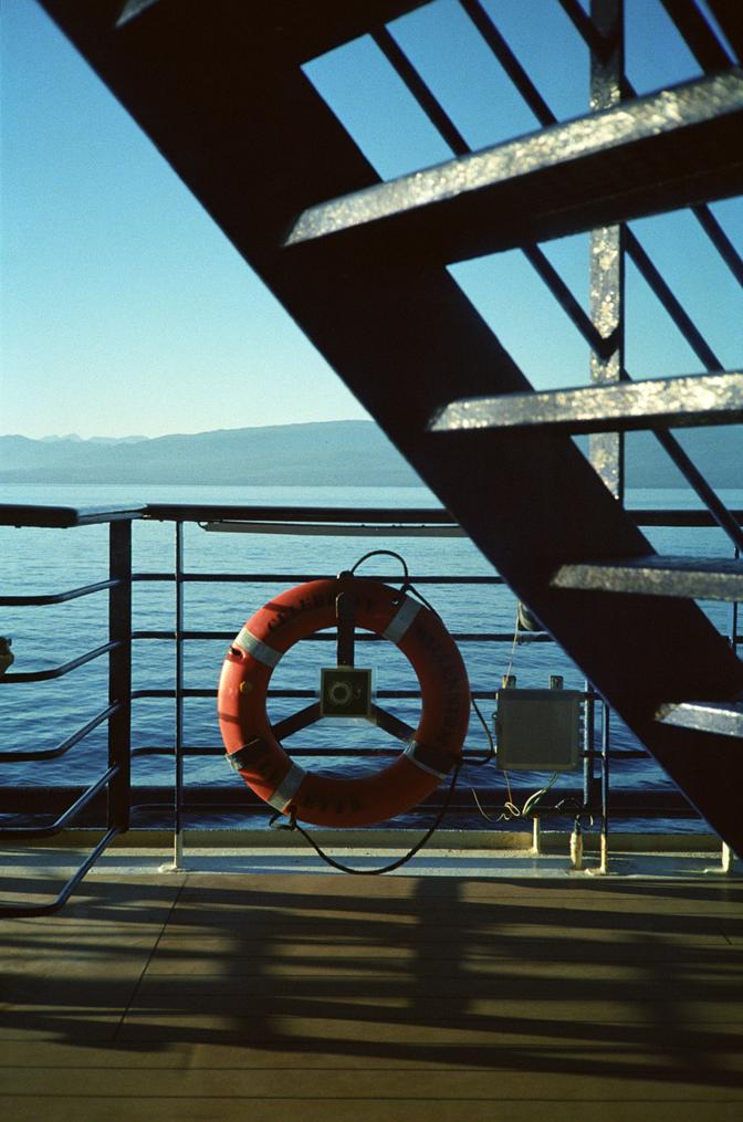 An emergency flotation device, mounted to the railing of a cruise ship, under the stairs, with the ocean in the background