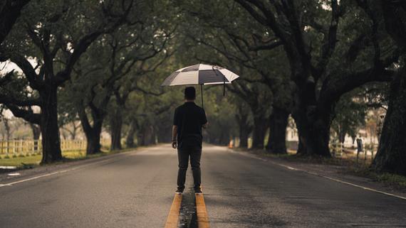 A man holding an umbrella, standing in the middle of the street